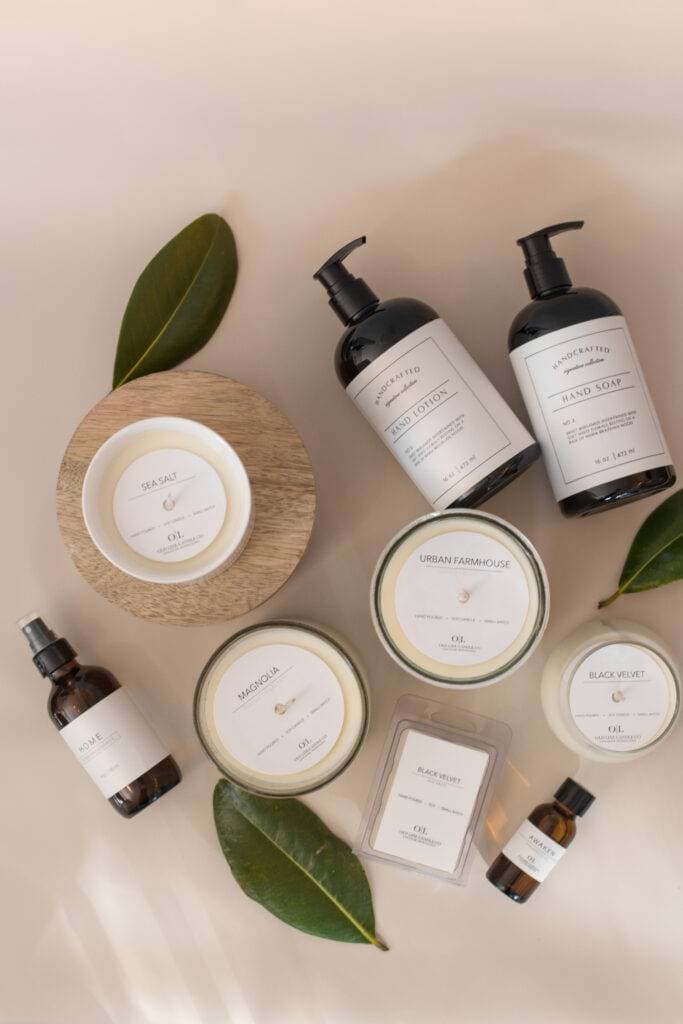 An overhead flat lay of Old Line Candle Co. candles, wax melts, room fragrance, fragrance oil, hand soap, and hand lotion arranged with green leaves.