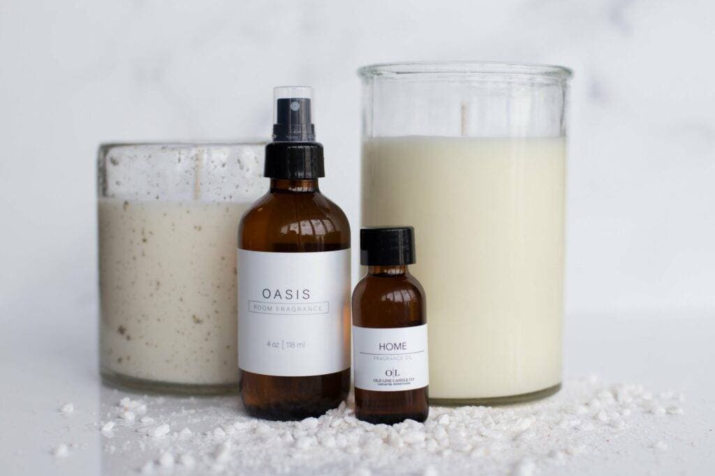 Old Line Candle Co. Oasis room fragrance and Home fragrance oil bottles beside a lit candle, surrounded by scattered wax melt pieces.